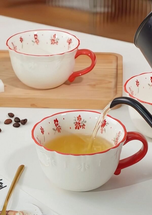White plastic high tea mug with red handle, red rim, and engraved floral pattern with red flowers and green leaves